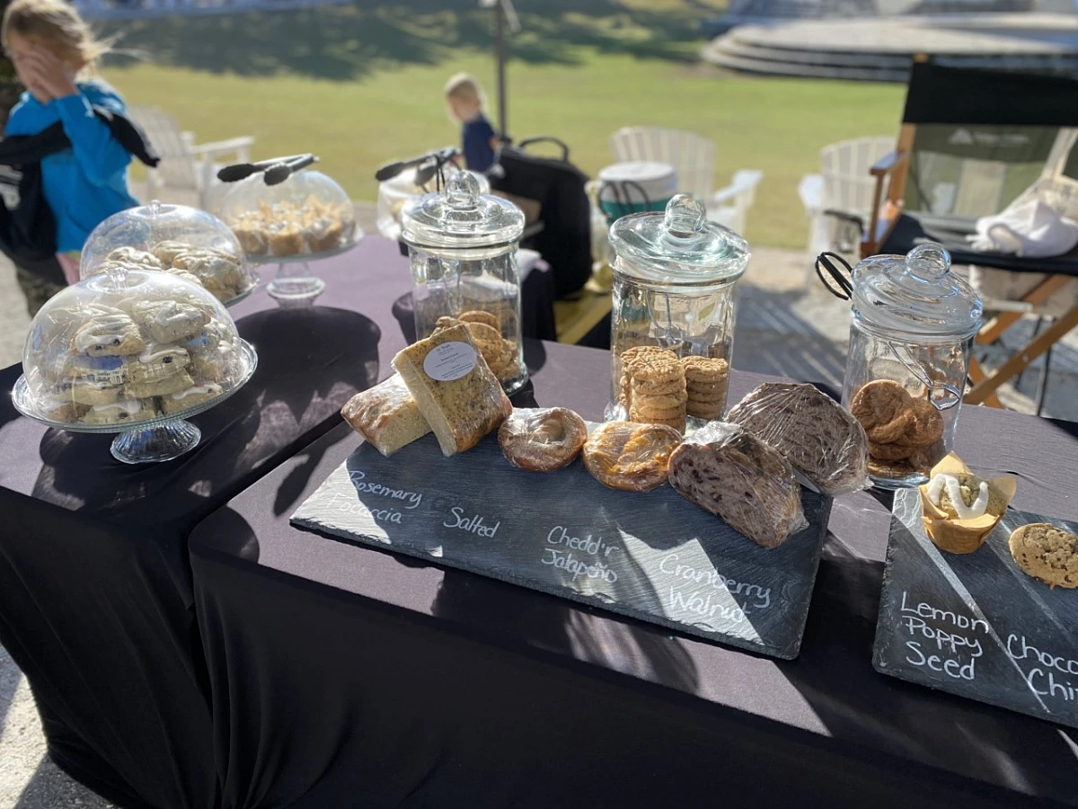 Outdoor table displaying assorted breads, cookies, and pastries in jars and domed stands.