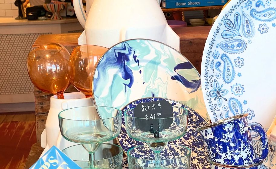 Display of colorful glassware and patterned plates arranged on wooden table in boutique.