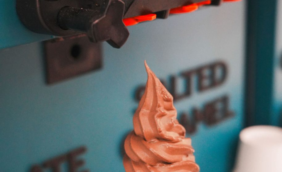 Chocolate soft-serve ice cream swirls from a teal frozen yogurt machine spout.