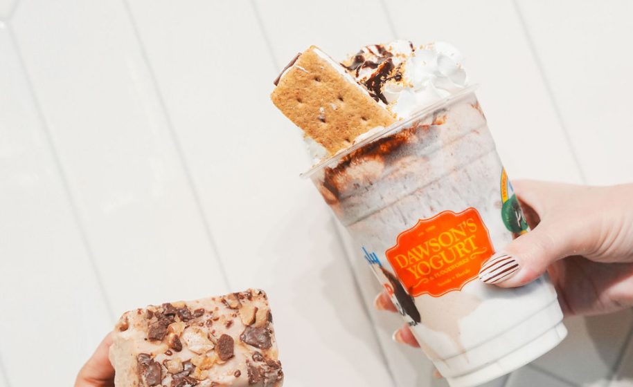 Hand holding s’mores-inspired frozen yogurt topped with graham cracker and chocolate drizzle.