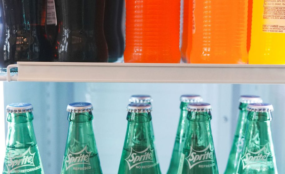 Assorted bottled sodas, including Sprite, neatly arranged inside refrigerated display.