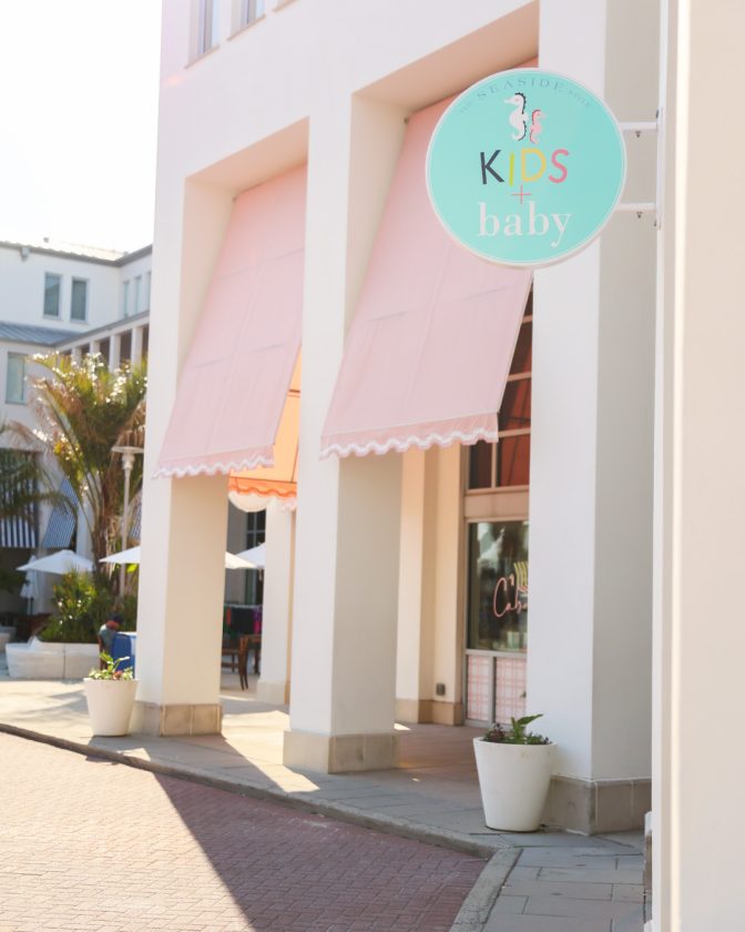 Pastel storefront with pink awnings and circular “Kids + Baby” sign hanging outside.