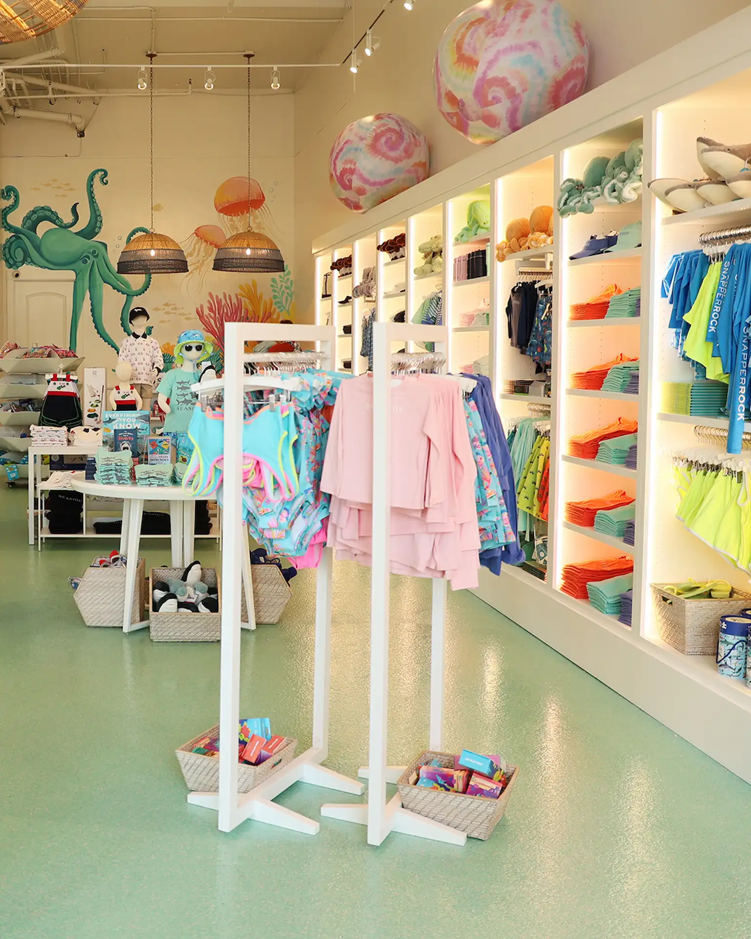 Bright, playful store interior with kids' swimwear, colorful displays, baskets, undersea mural and oversized beach balls.