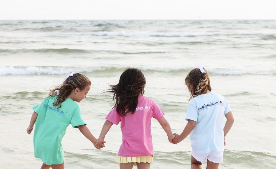 Three young girls in colorful Seaside Florida holding hands as they wade into the gentle surf on the beach in Seaside, Florida