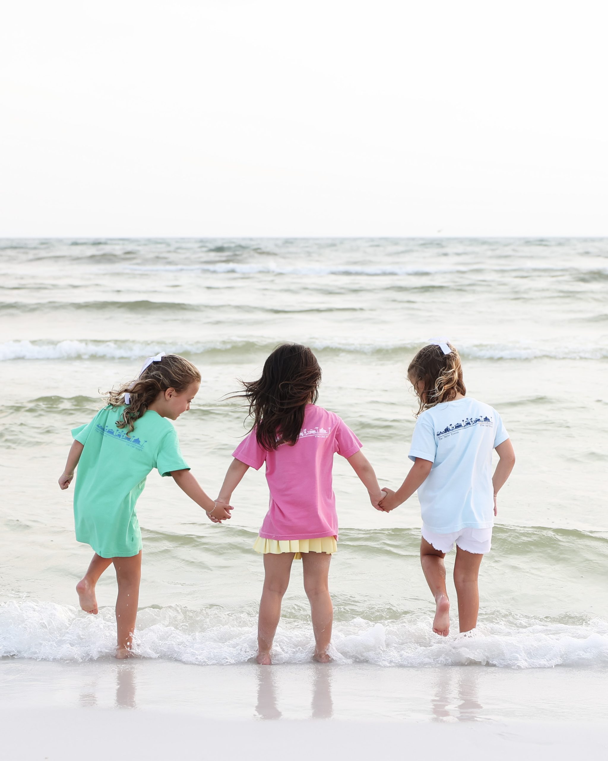 Three young girls in colorful Seaside Florida holding hands as they wade into the gentle surf on the beach in Seaside, Florida
