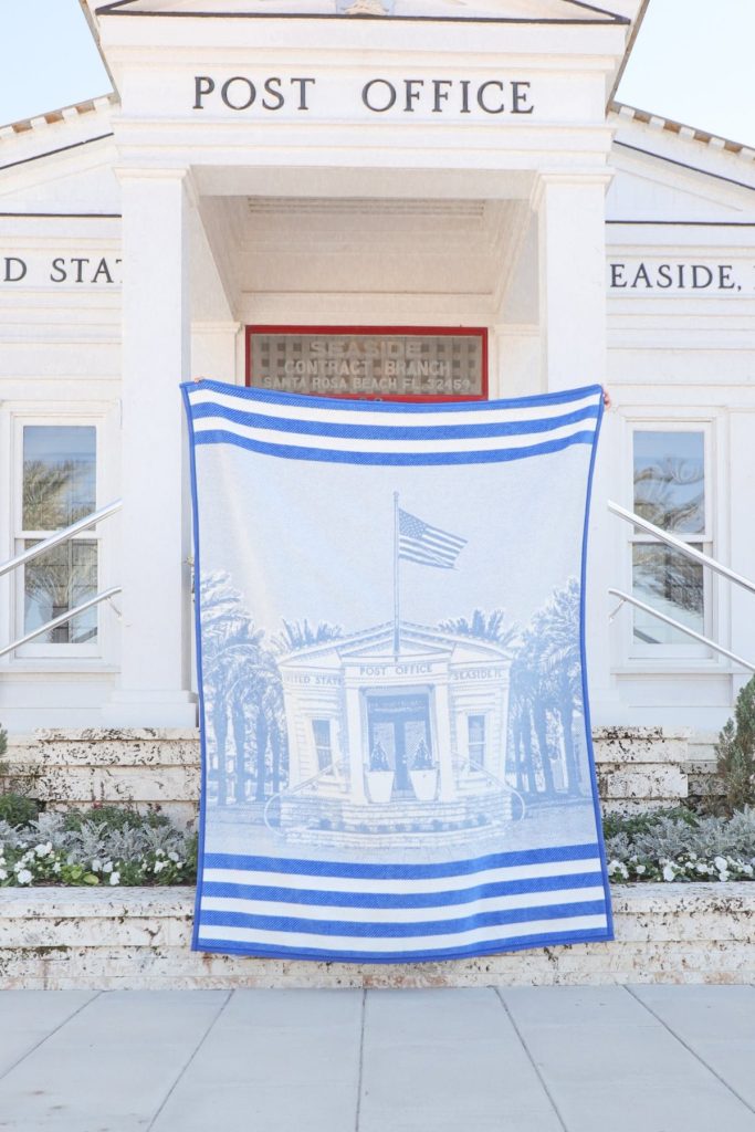 Blue and white striped blanket with post office illustration displayed on stone steps in front of building.