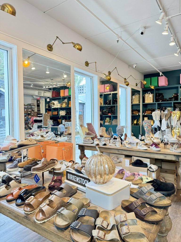 Stylish boutique displaying Birkenstock sandals and designer shoes on wooden tables with handbags and decor.