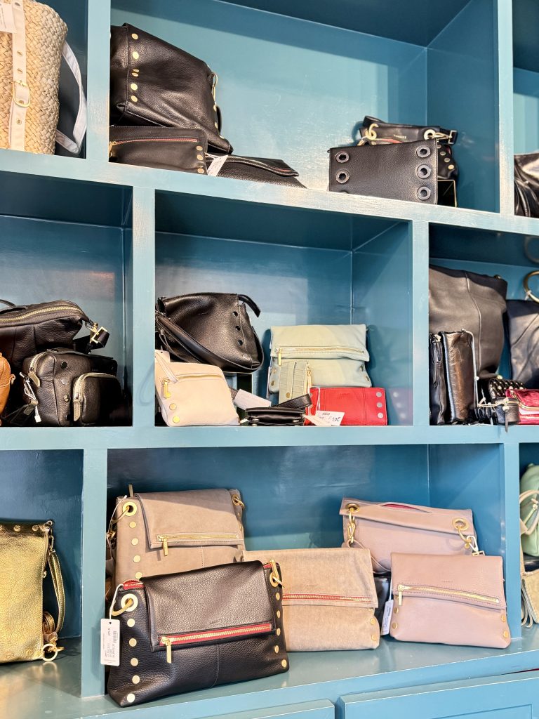 Various stylish handbags in black, beige, and pastel colors displayed on blue shelves inside a boutique store.