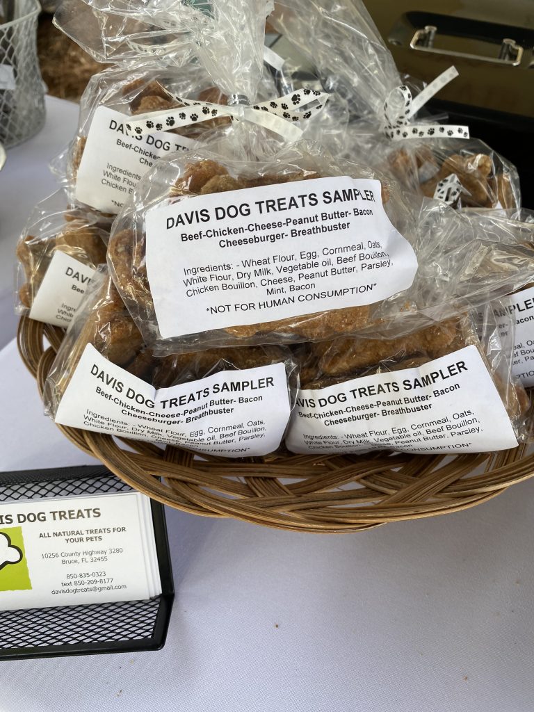 Basket of packaged Davis Dog Treats samplers with labeled ingredients, displayed on a vendor table.