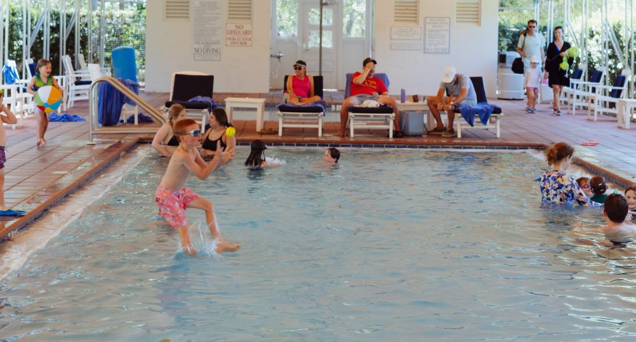 Children and adults playing and relaxing around an indoor pool with lounge chairs and toys.