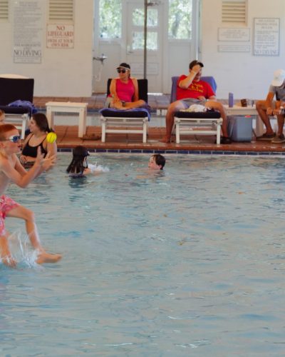 Children and adults playing and relaxing around an indoor pool with lounge chairs and toys.
