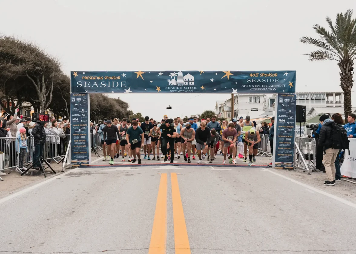 Runners launching from starting line beneath Seaside-sponsored race banner, crowd cheering nearby.