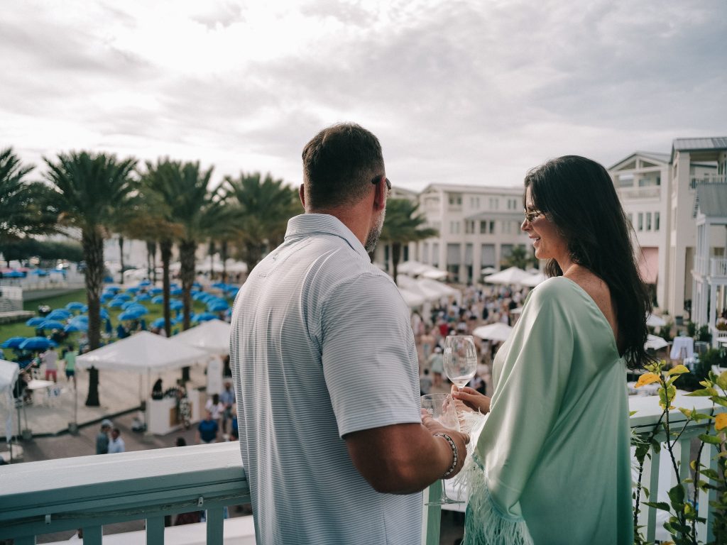 Couple enjoying drinks on balcony overlooking lively outdoor market.