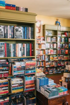 Bookshelves and stacked novels inside a cozy independent bookstore.