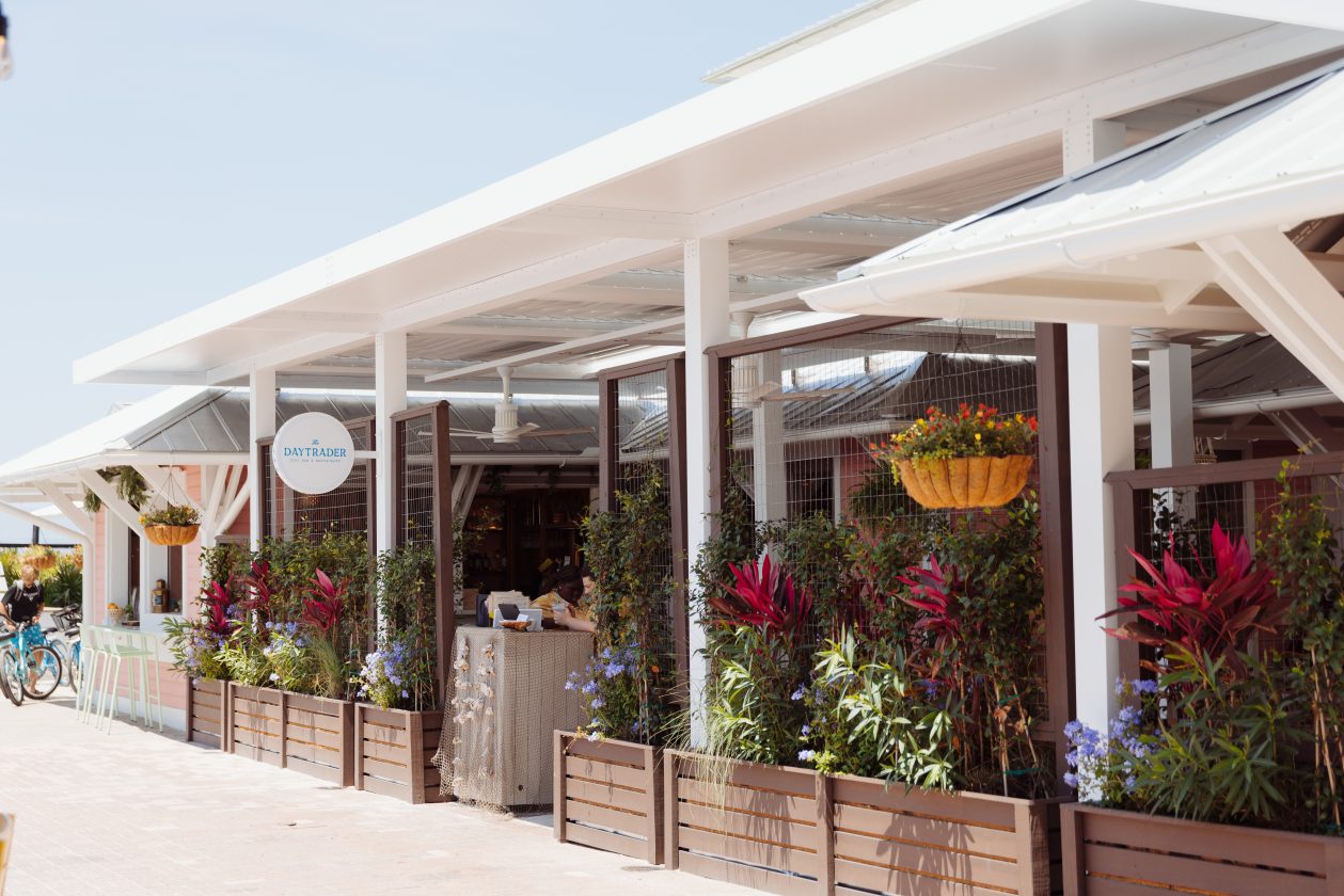 Outdoor café with white canopy, green plants, red flowers, wooden planters, and a bicycle nearby.