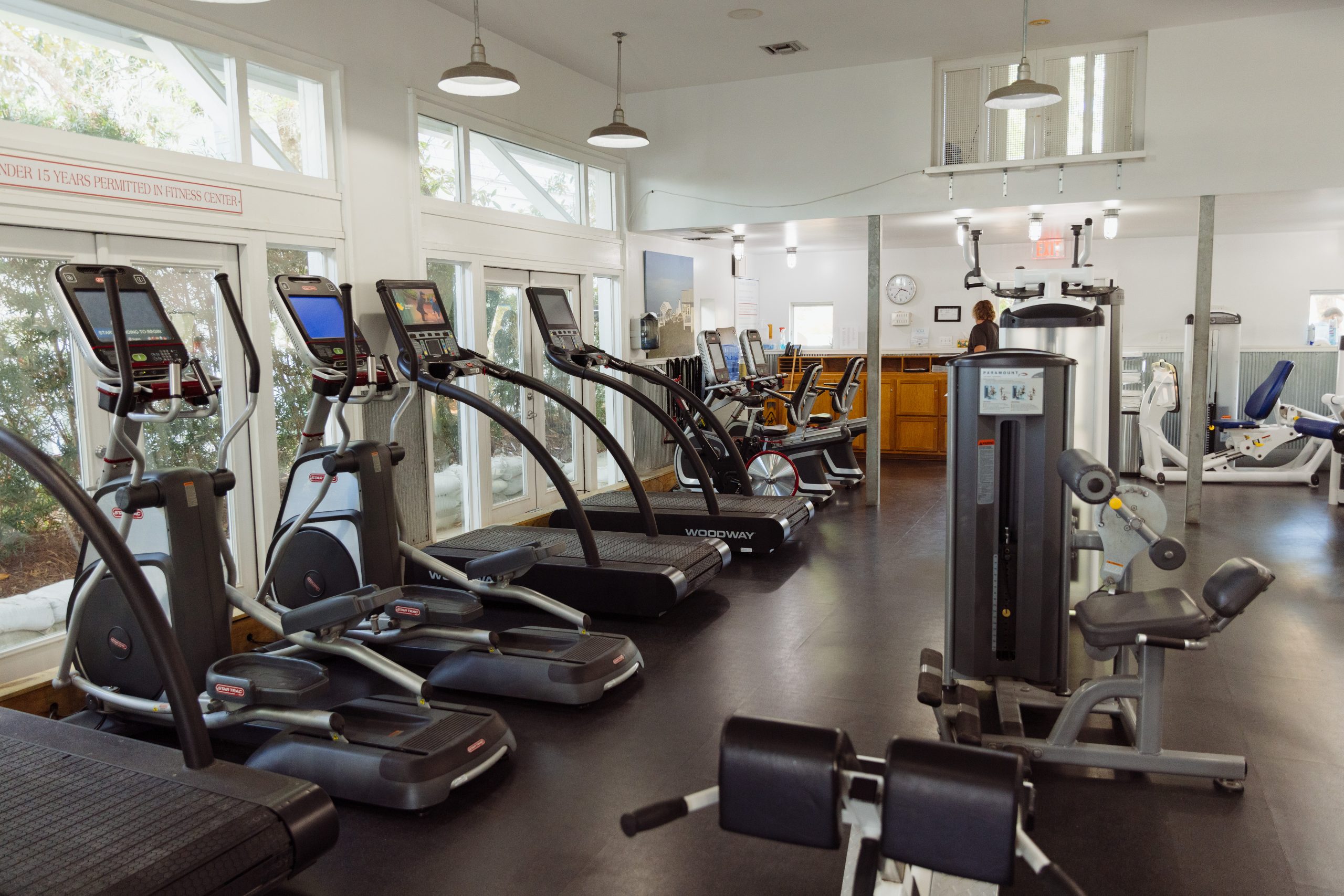 Bright, modern gym with treadmills, ellipticals, and strength machines lined up by large windows.