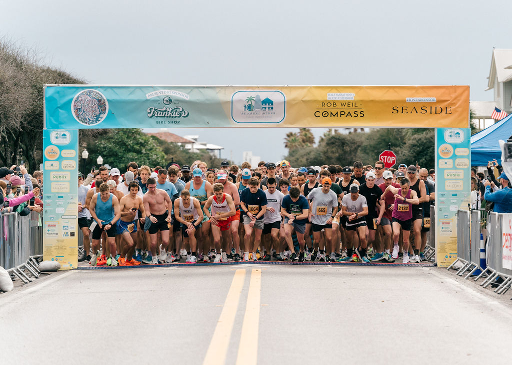 Runners launching from the starting line of a coastal road race.