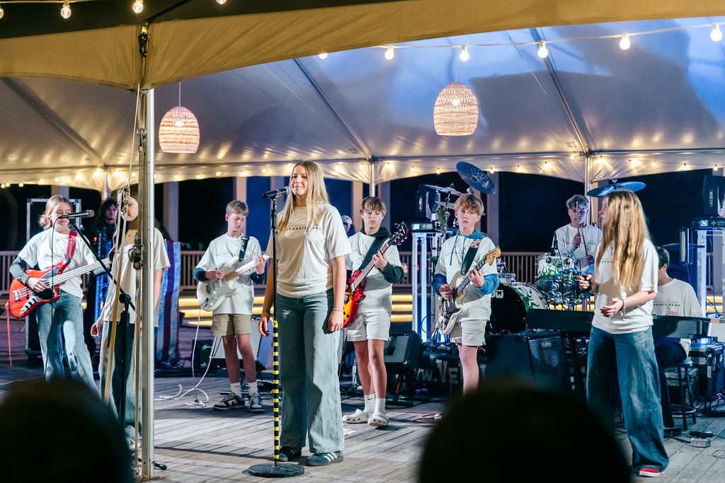 Youth band performing live on an outdoor stage under string lights.