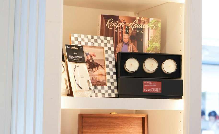 Shelf displays Ralph Lauren book, three white candles in black box, bracelet, and cowboy photograph in frame.