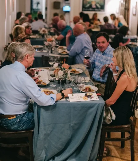 Guests seated at a long table enjoying dinner and conversation at a warmly lit restaurant gathering