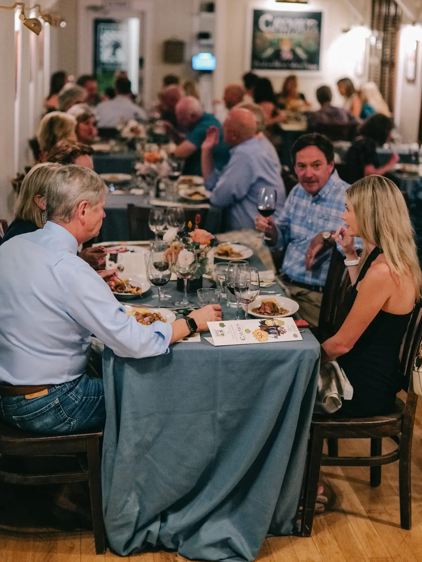 Guests seated at a long table enjoying dinner and conversation at a warmly lit restaurant gathering