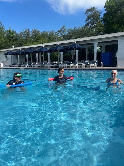 Three people enjoying water exercise in an outdoor swimming pool.