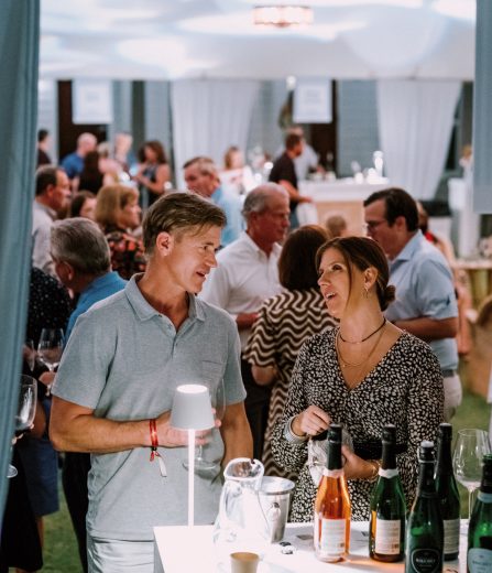 Guests socializing at an indoor wine tasting event with bottles displayed on a glowing table.