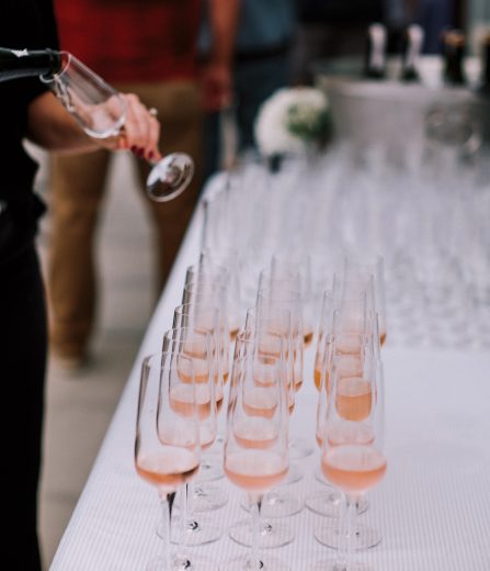 Sparkling rosé being poured into rows of champagne flutes at an event.