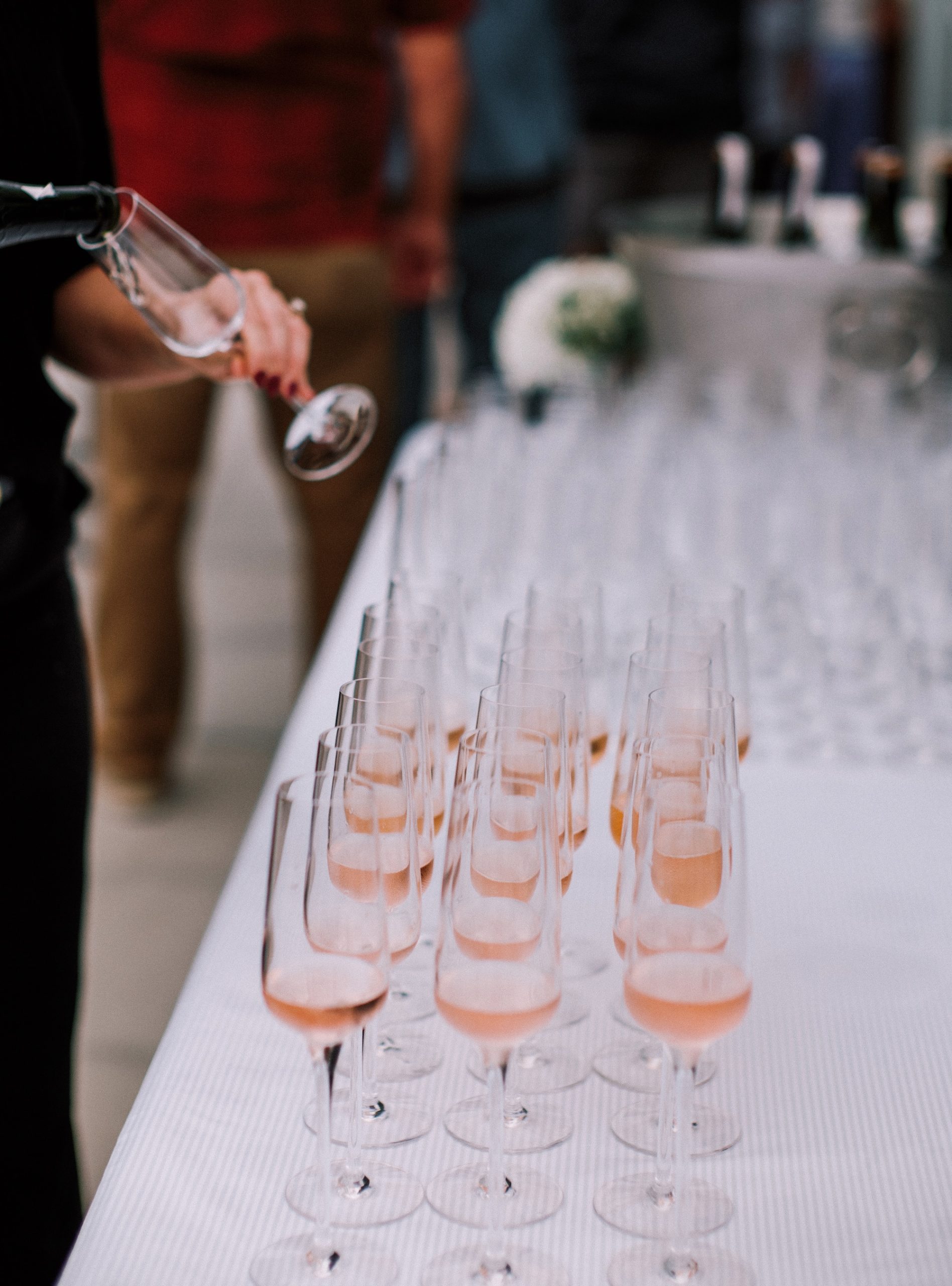 Sparkling rosé being poured into rows of champagne flutes at an event.
