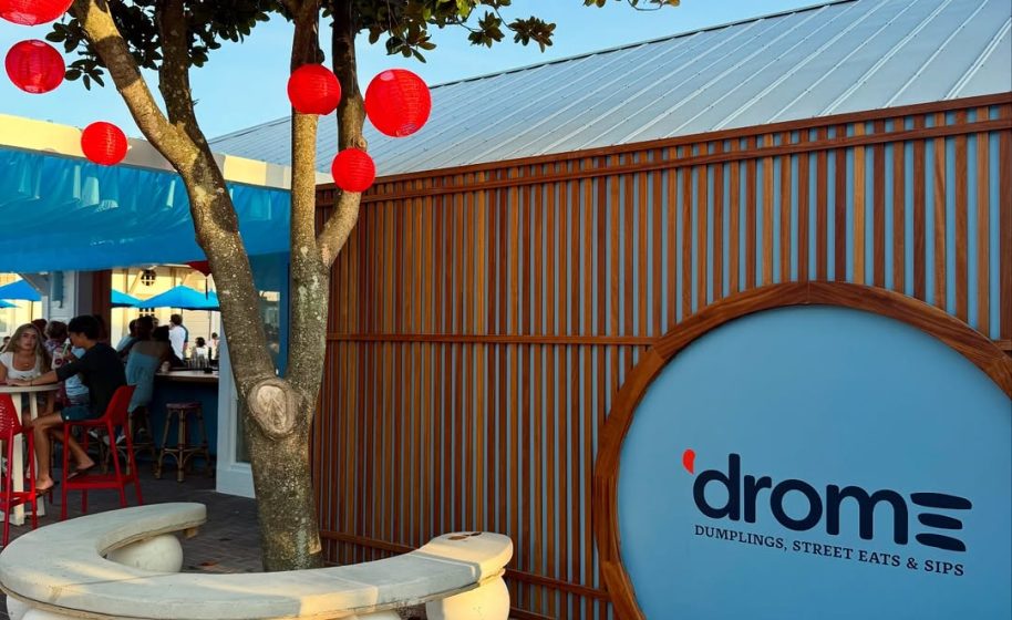 Outdoor restaurant with red lanterns, wooden decor, and sign reading ‘drome: dumplings, street eats & sips.