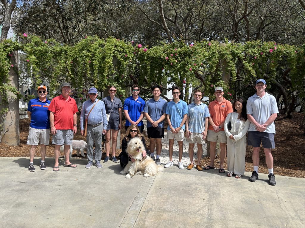 Large family group with two dogs posing on sunny path beneath flowering green vine-covered trellis.