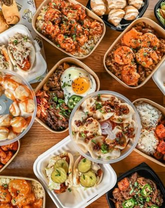 Assorted Asian-inspired dishes including rice bowls, dumplings, and bao buns arranged on a wooden table.