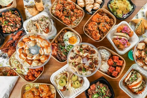 Assorted Asian-inspired dishes including rice bowls, dumplings, and bao buns arranged on a wooden table.