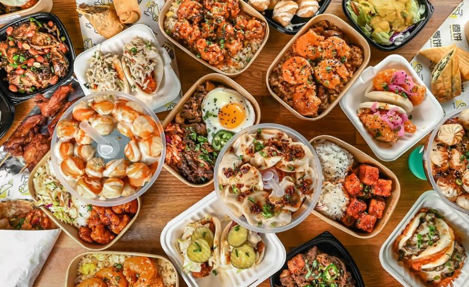 Assorted Asian-inspired dishes including rice bowls, dumplings, and bao buns arranged on a wooden table.