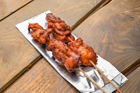 Two skewers of grilled marinated meat served on foil, resting on a rustic wooden table.