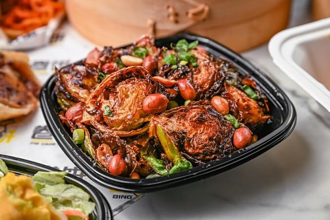 Crispy roasted Brussels sprouts in black bowl, garnished with peanuts, scallions, and flavorful dark sauce.
