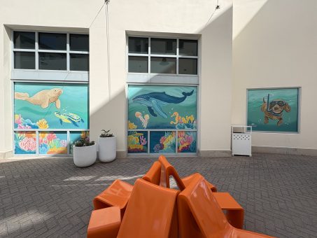 Colorful ocean-themed murals featuring sea animals on windows above bright orange geometric outdoor seating.