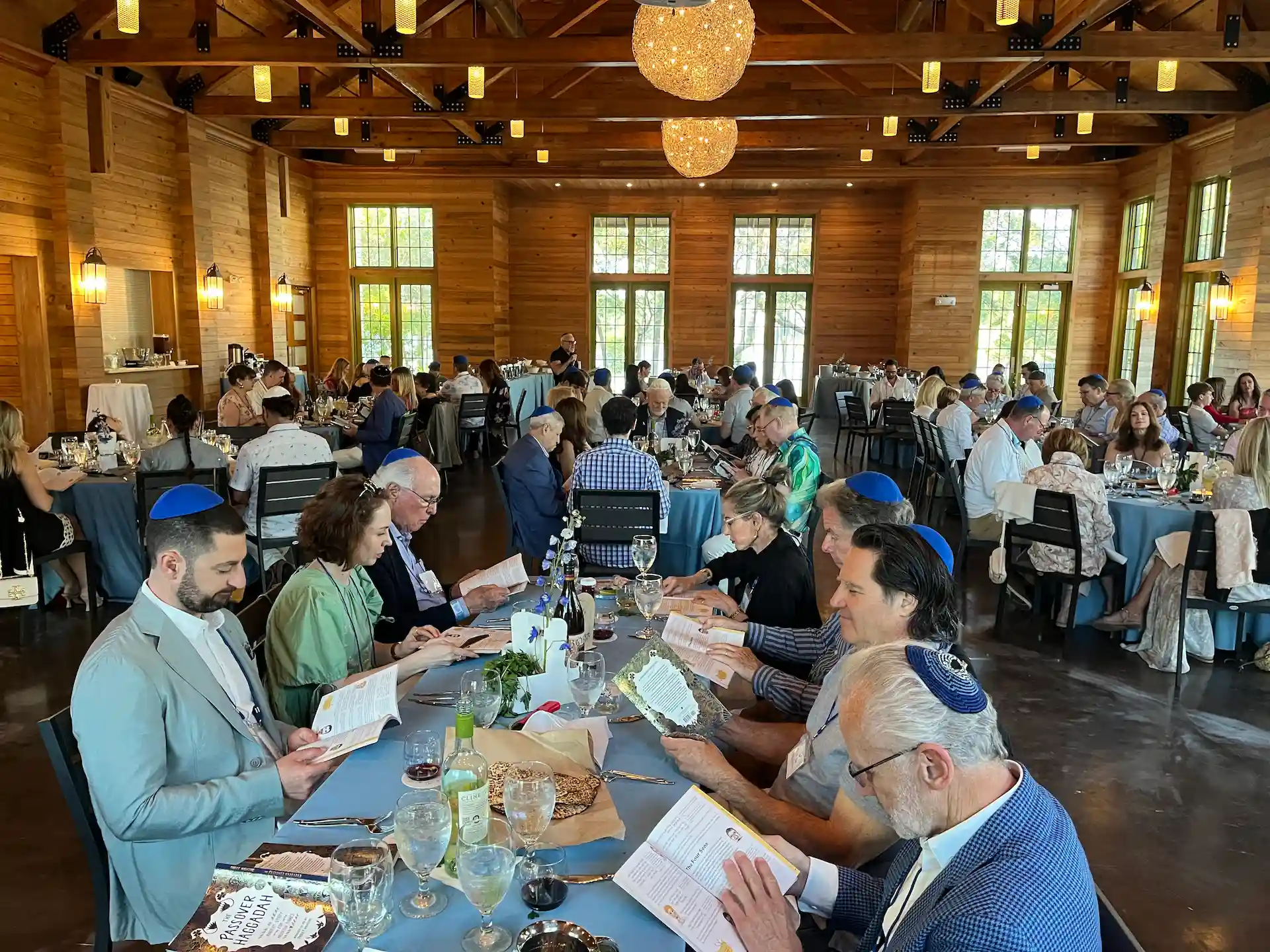 Large group dining inside a wooden event hall, guests seated at tables reading programs during a formal gathering.
