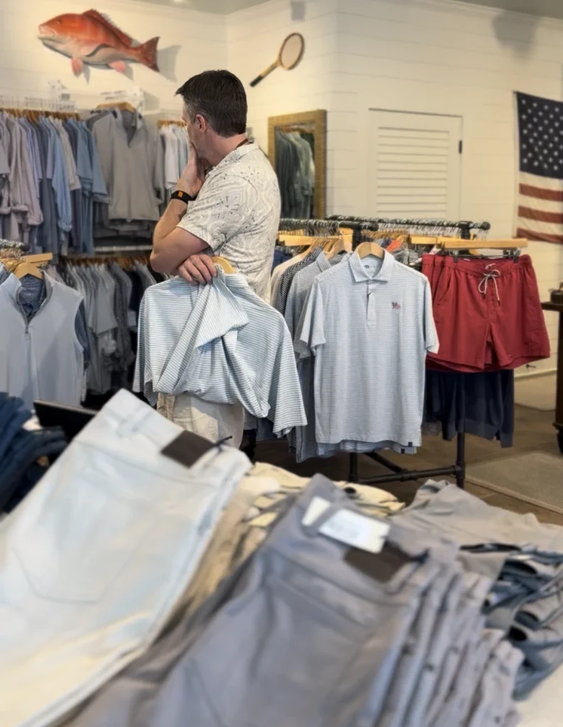 Man shopping for shirts in casual menswear store, surrounded by racks with clothing and folded pants.