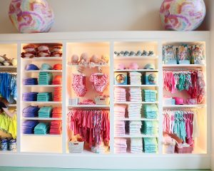 Colorful boutique display with neatly folded swimwear, towels, and accessories in pink, blue, and turquoise.