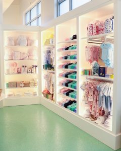 Colorful store shelves display neatly stacked children’s clothes, hats, boxes, and baby items in a bright space.