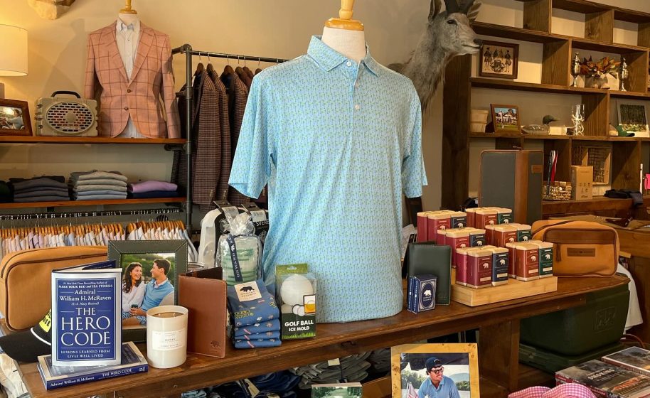 Men’s clothing store with light blue polo displayed on mannequin, golf accessories, shirts and decor including animal mounts.