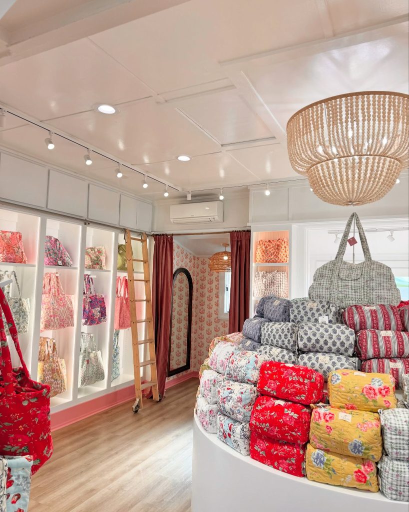 Bright boutique interior displays colorful floral bags and pouches on shelves with wooden floor and ceiling lights.