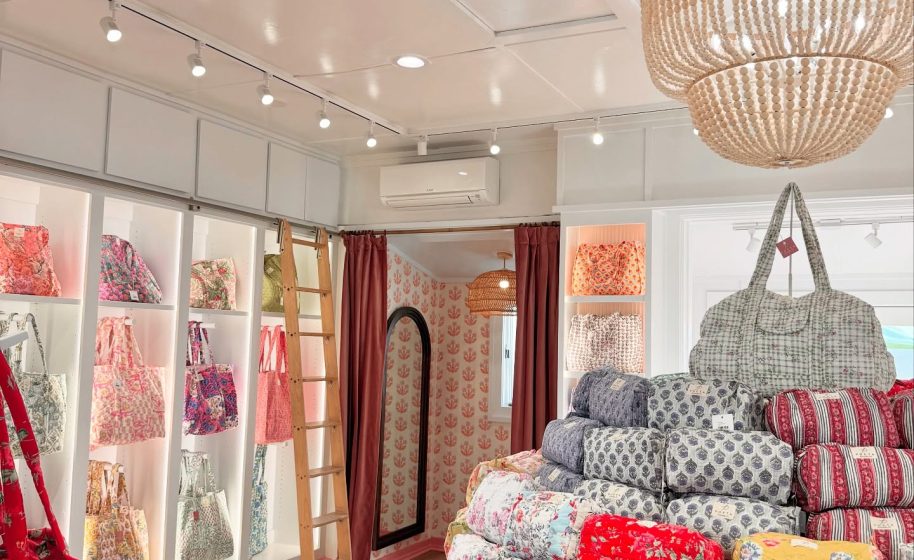 Bright boutique interior displays colorful floral bags and pouches on shelves with wooden floor and ceiling lights.