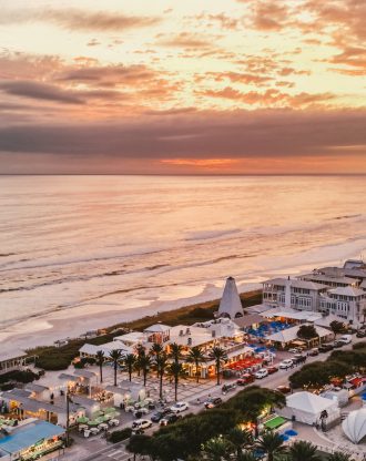 Aerial view of seaside town at sunset with beachfront buildings and glowing shoreline.