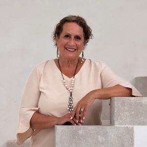 Smiling woman in light pink blouse and necklace posing on light stone staircase indoors.