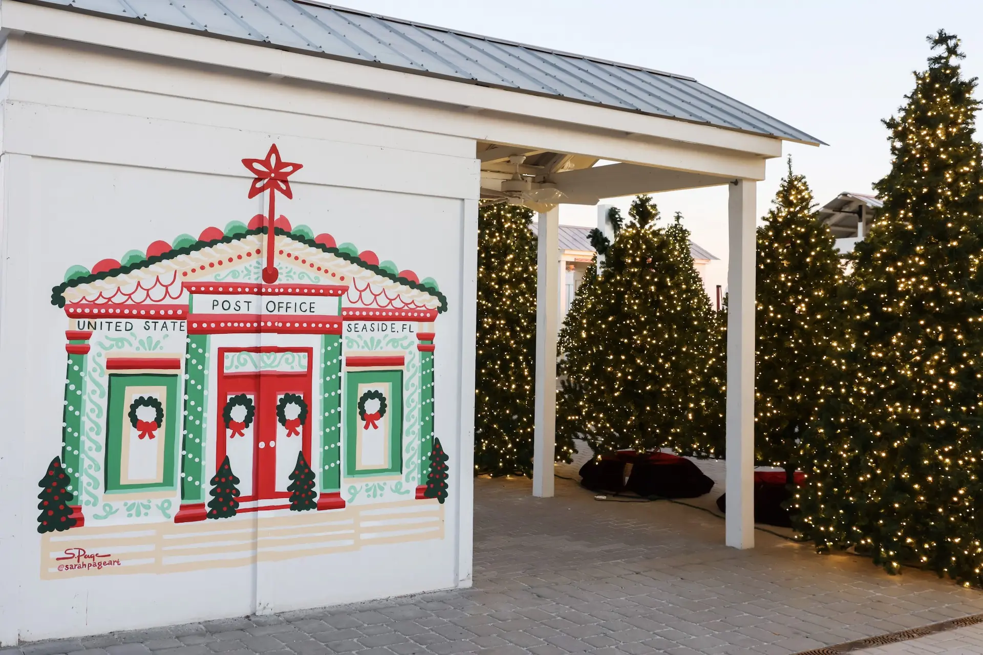 Festive mural of a post office with decorated Christmas trees covered in twinkling lights beside it.