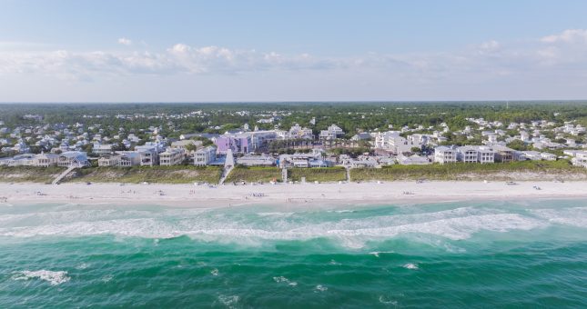 Aerial view of coastal town with beachfront homes, sandy shoreline, and turquoise ocean waves.