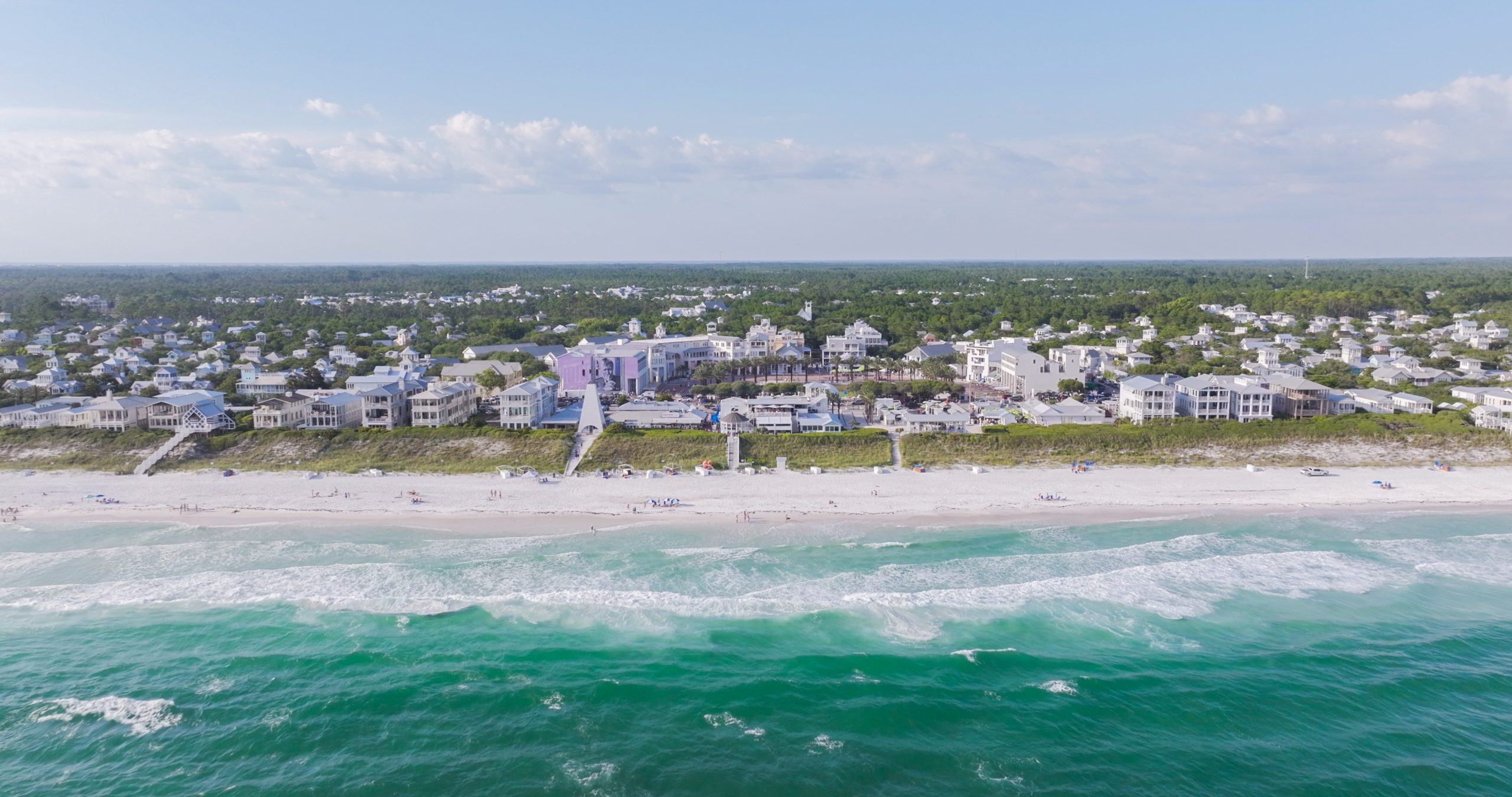 Aerial view of coastal town with beachfront homes, sandy shoreline, and turquoise ocean waves.