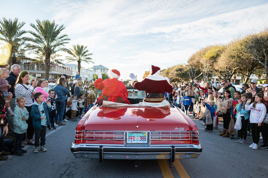 Santa and Mrs. Claus waving from convertible during festive holiday parade.